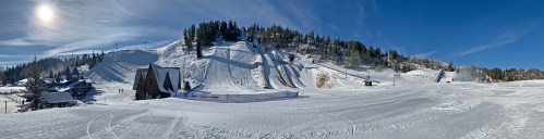 A panoramic view of a snowy ski resort with slopes, trees, and a clear blue sky.