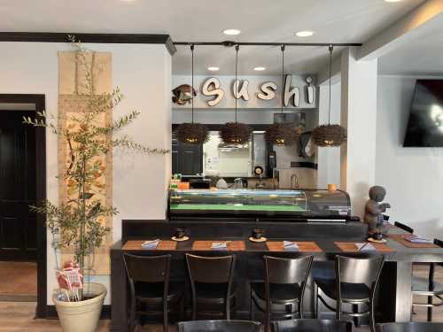 A modern sushi restaurant interior featuring a sushi bar, decorative plants, and stylish pendant lighting.