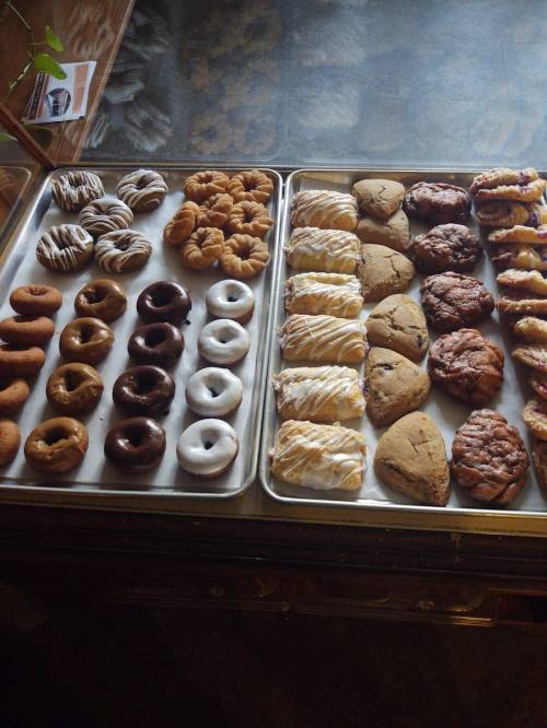A display of assorted baked goods, including donuts, pastries, and cookies on trays.