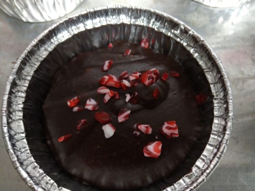 A chocolate dessert in a foil cup, topped with red and white peppermint pieces.