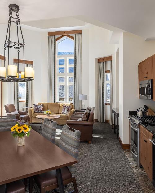 Bright, modern kitchen and living area with large windows, a dining table, and cozy seating, featuring sunflowers on the table.