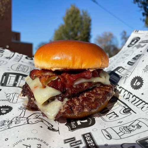 A juicy burger with melted cheese and crispy bacon, served on a toasted bun, resting on patterned paper.