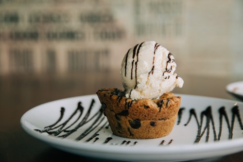 A warm chocolate chip cookie cup topped with a scoop of vanilla ice cream and drizzled with chocolate sauce.