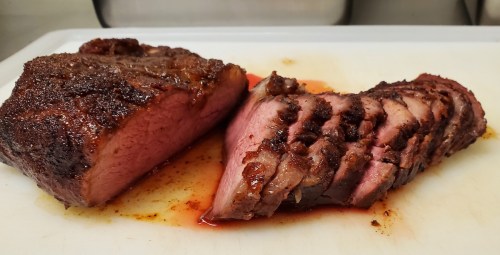 Sliced smoked meat on a cutting board, showcasing a juicy interior and a flavorful, charred exterior.