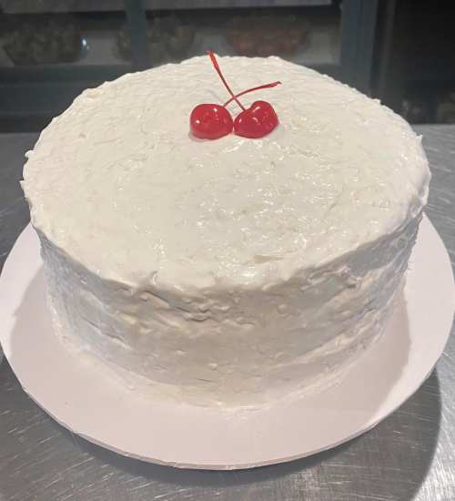 A round white cake topped with two red cherries, placed on a white cake board.
