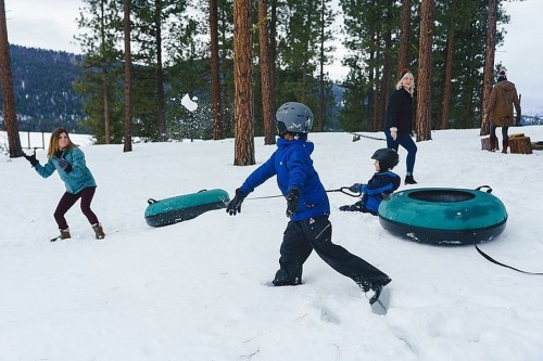 A snowy scene with children playing and tubing, while adults enjoy the winter landscape in the background.