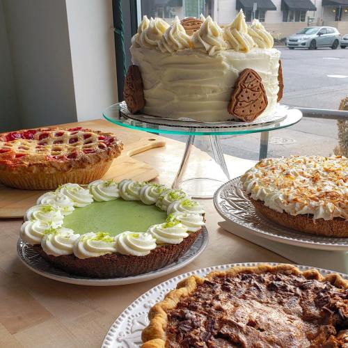 A display of various desserts: a layered cake, a lime pie, a chocolate pie, and a fruit pie, all beautifully presented.