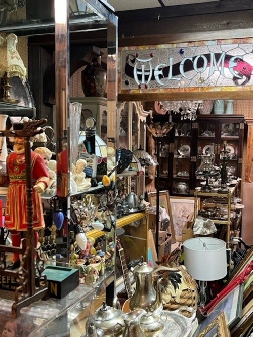 A cozy antique shop filled with various collectibles, decor, and a "Welcome" sign overhead.