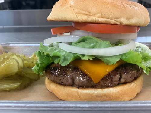 A close-up of a cheeseburger with lettuce, tomato, onion, and pickles on a tray.