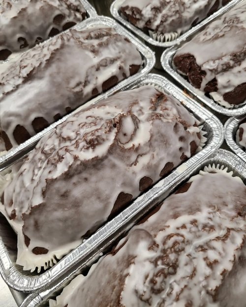 Freshly baked loaves of cake with a glossy white icing, arranged in aluminum trays.