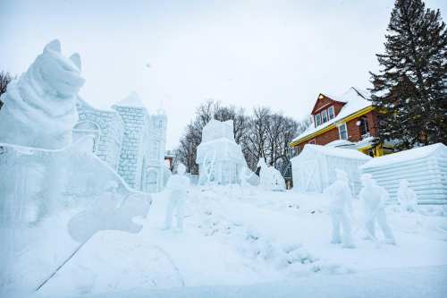A winter scene featuring intricate snow sculptures, including animals and structures, set against a snowy landscape.