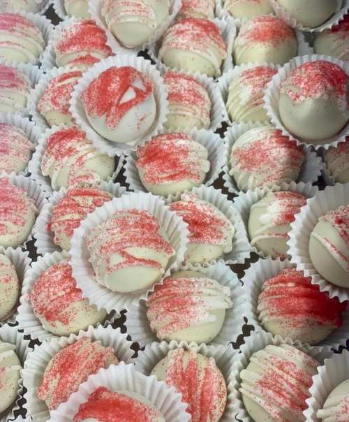 A close-up of white chocolate truffles with red sprinkles, arranged in paper cups on a tray.