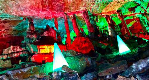 Colorful illuminated cave with vibrant red, green, and blue lights highlighting rock formations and stalagmites.