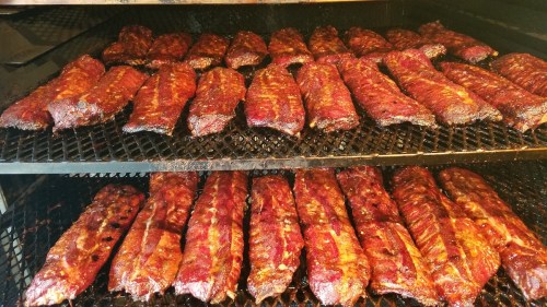 A close-up of multiple racks of smoked ribs, glistening with a rich, dark glaze, arranged neatly in a smoker.
