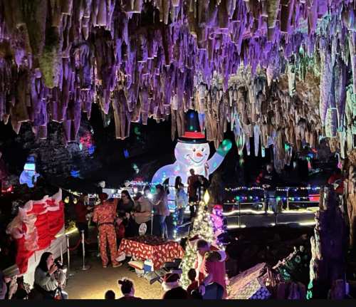 A festive cave scene with colorful lights, a snowman, and visitors enjoying holiday decorations and activities.
