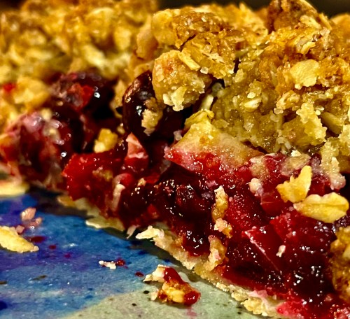 Close-up of a slice of cherry pie with a crumbly oat topping on a colorful plate.
