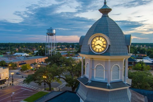 A clock tower at sunset, with a water tower in the background and a view of a small town below.