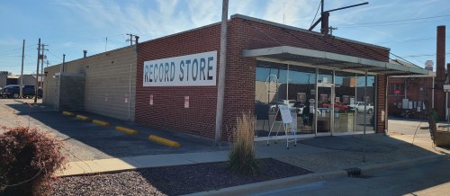 A brick building with a large sign reading "RECORD STORE" and glass doors, set against a clear blue sky.