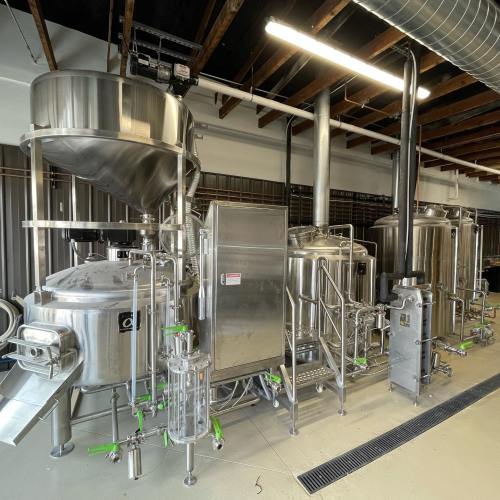 A modern brewing setup featuring stainless steel tanks and pipes in a spacious industrial environment.