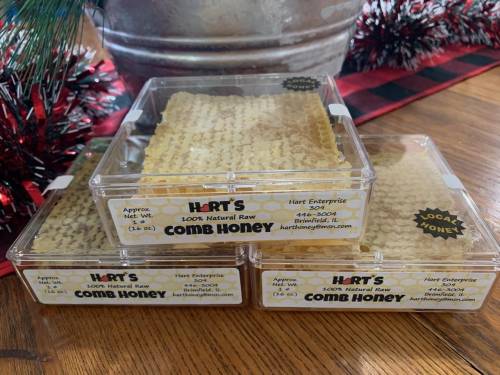 Three clear containers of comb honey stacked on a wooden surface, with festive decorations in the background.