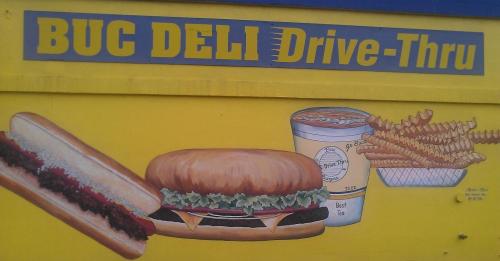 Colorful mural featuring a hot dog, burger, fries, and a drink with "Buc Deli Drive-Thru" text above.