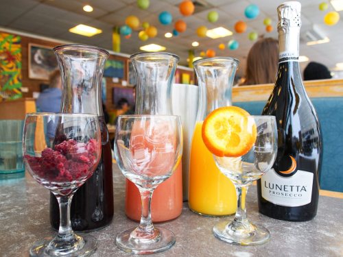 A table with three carafes of colorful drinks and a bottle of Lunetta Prosecco, garnished with an orange slice.