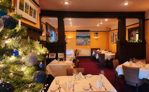 Cozy restaurant interior decorated for the holidays, featuring tables set with white linens and a festive Christmas tree.