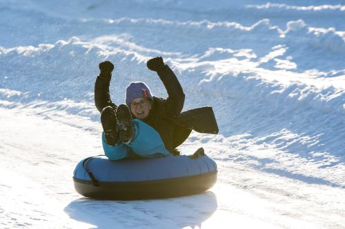 A person joyfully tubing down a snowy slope, raising their arms in excitement.