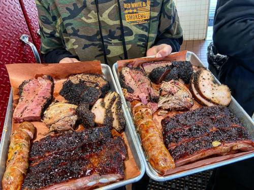 Two trays of assorted smoked meats, including brisket, sausage, and ribs, served with slices of bread.