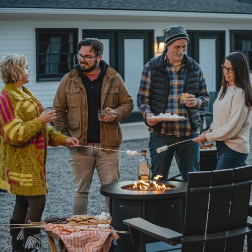 A group of friends gathered around a fire pit, roasting marshmallows and enjoying drinks in a cozy outdoor setting.