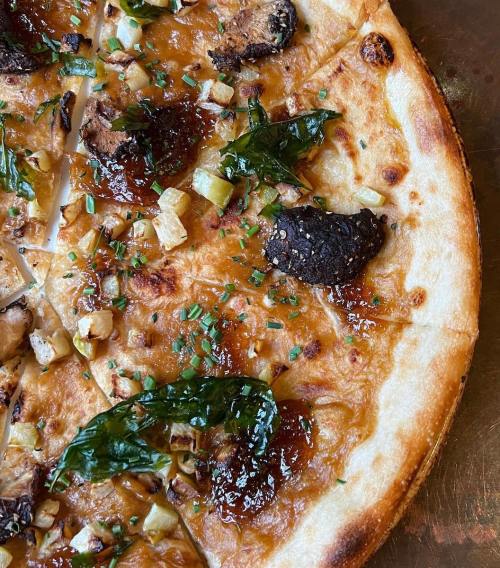 Close-up of a gourmet pizza topped with mushrooms, herbs, and caramelized onions on a crispy crust.
