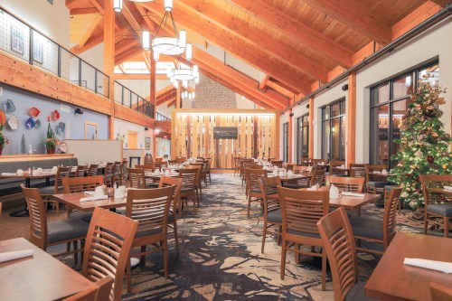 A spacious restaurant with wooden beams, tables set for dining, and a Christmas tree in the corner.