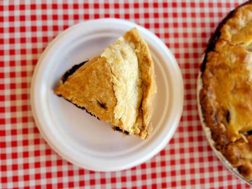 A slice of pie on a white plate, resting on a red and white checkered tablecloth.