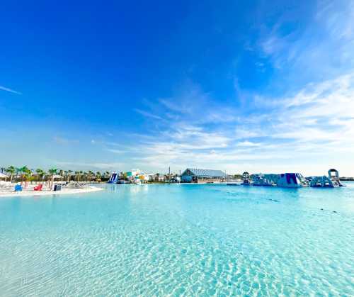 A serene beach scene with clear blue water, palm trees, and inflatable water attractions under a bright sky.