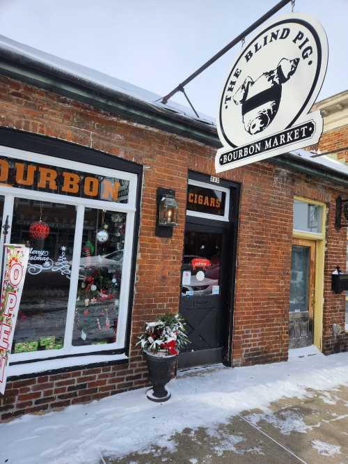 Exterior of The Blind Pig Bourbon Market, featuring a brick facade, a sign, and snow on the ground.