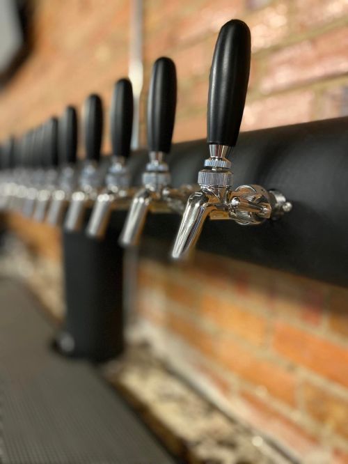 A row of shiny beer taps with black handles against a brick wall.