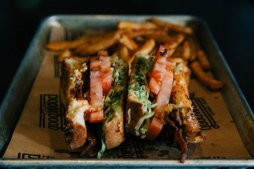 A close-up of a sandwich with lettuce, tomato, and bacon, served with a side of fries on a metal tray.