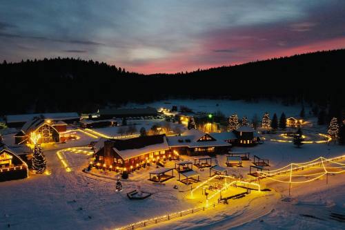 A snowy landscape at dusk, featuring a cozy lodge and illuminated pathways lined with festive lights and trees.