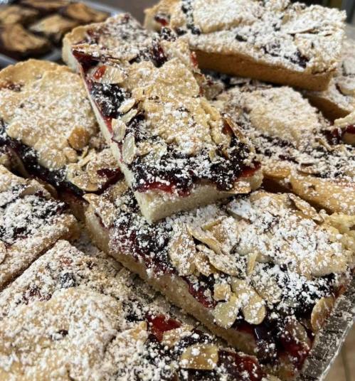 A close-up of dessert bars topped with powdered sugar, oats, and a layer of fruit filling, stacked on a tray.