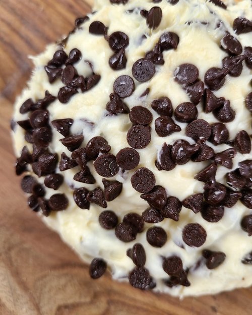 Close-up of a creamy dessert topped with a generous layer of chocolate chips on a wooden surface.