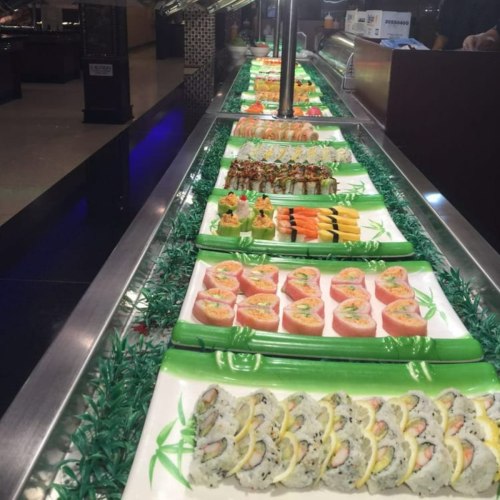 A variety of colorful sushi rolls displayed on green trays at a buffet.