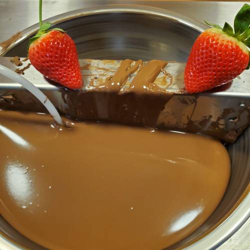 A bowl of melted chocolate with two strawberries resting on the edge, ready for dipping.
