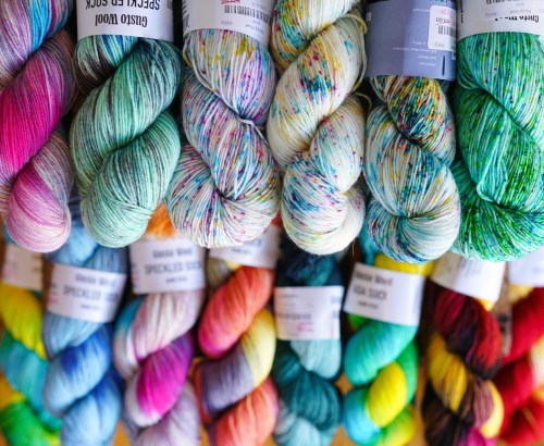 A colorful display of various yarn skeins in vibrant shades, including pink, green, yellow, and blue, stacked together.