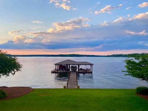 A serene lakeside view featuring a dock extending into calm waters under a colorful sunset sky.