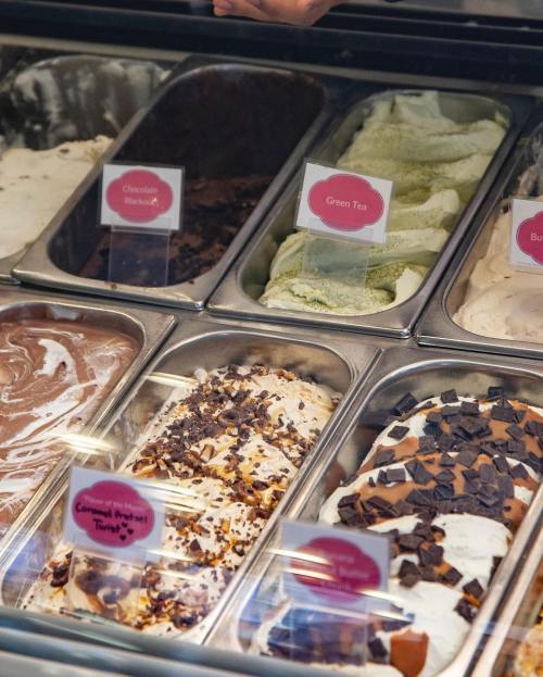 A display of various ice cream flavors in metal tubs, including chocolate, green tea, and caramel pretzel.