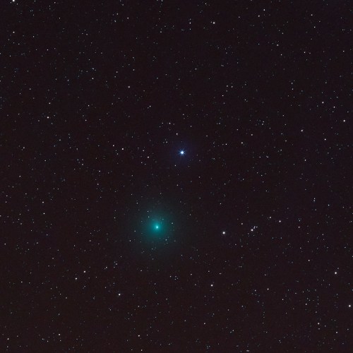 A dark night sky filled with stars, featuring a bright blue star and a glowing green comet.