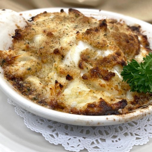 A baked dish with a golden, crispy topping, featuring creamy white filling and garnished with a parsley sprig.