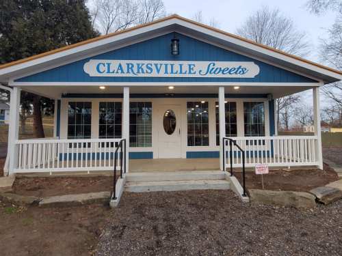 A blue and white building with "Clarksville Sweets" sign, featuring a porch and large windows.