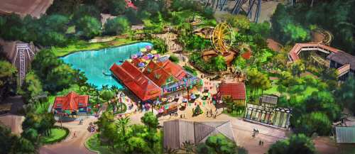 Aerial view of a vibrant amusement park with a lake, rides, and colorful buildings surrounded by lush greenery.
