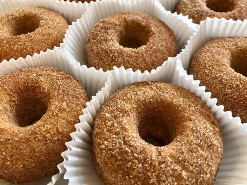 A close-up of freshly baked donuts coated in cinnamon sugar, arranged in white paper liners.
